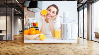 Cheerful woman showing half of orange sitting on kitchen Wall mural