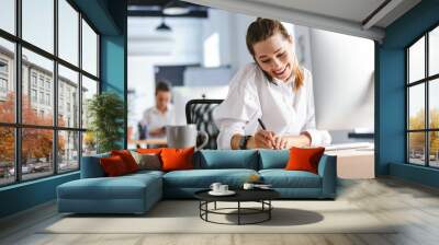 cheerful young businesswoman sitting at her workplace Wall mural