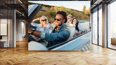 Cheerful young friends driving car and smiling in summer Wall mural