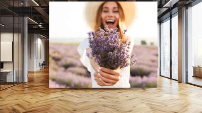 Cheerful young girl in straw hat holding lavender bouquet Wall mural