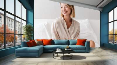 Cheery young woman indoors on bed at home. Wall mural