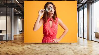 Close-up portrait of surprised beautiful woman looking at camera through magnifying glass Wall mural