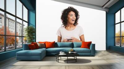 Communicating woman with afro hairstyle using mobile phone and looking aside on copyspace, isolated over white background Wall mural