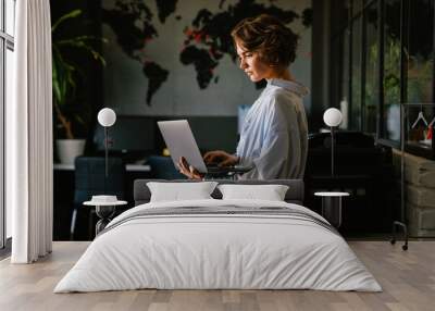 Concentrated business woman using laptop while standing in modern workspace Wall mural