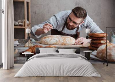 concentrated man baker standing at bakery near bread. Wall mural