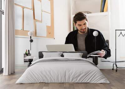 Concentrated professional man architect in office reading book work with paper using laptop computer. Wall mural