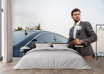 Confident young businessman in suit opens his car Wall mural