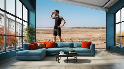 Confident young sportsman standing at beach Wall mural