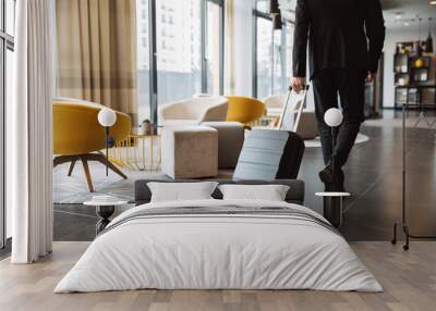 Cropped photo of caucasian businessman wearing suit walking with suitcase in hotel lobby Wall mural