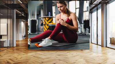 Displeased young woman fitness coach with pain in her leg Wall mural