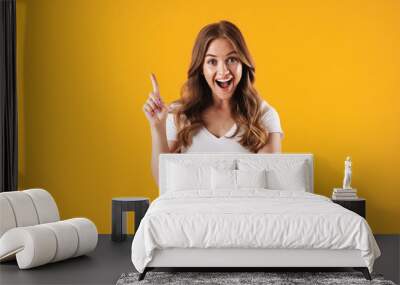 Emotional happy girl in casual white t-shirt posing isolated over yellow wall background have an idea pointing. Wall mural