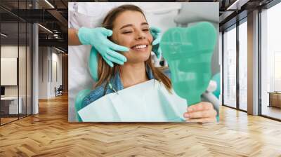 European young woman smiling while looking at mirror in dental clinic Wall mural