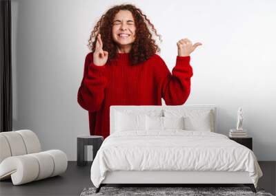 Excited girl holding fingers crossed and pointing finger aside Wall mural