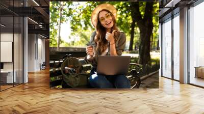 Excited happy woman outdoors sitting using laptop computer make thumbs up. Wall mural