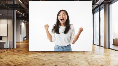 Excited pretty young asian woman showing winner gesture. Wall mural