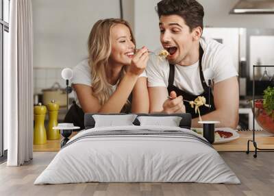 Excited young friends loving couple chefs on the kitchen eat tasty pasta. Wall mural