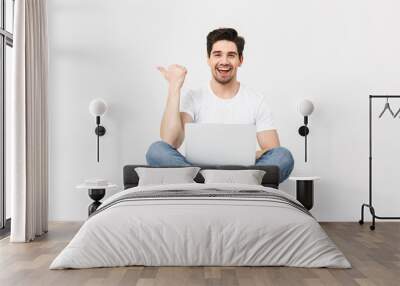 Excited young man posing isolated over white wall using laptop computer pointing sitting on floor. Wall mural