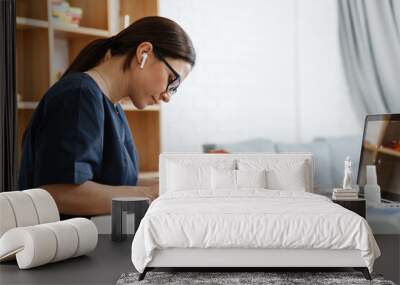 Focused woman doctor using earphone while working with laptop and papers Wall mural