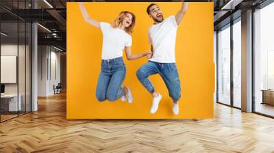 Full length image of cheerful couple rejoicing and jumping while taking selfie photo on cellphone Wall mural