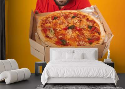 Full length image of optimistic delivery man in red uniform smiling and holding pizza box Wall mural