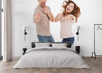 Full-length photo of cheerful loving couple in casual t-shirt and jeans jumping and pointing index fingers on camera like hey you with candid smile, isolated over white background Wall mural