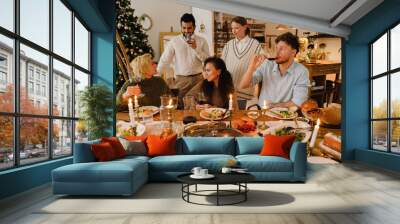 Group of joyful friends having traditional dinner together during Christmas holidays Wall mural