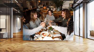 Group of smiling friends clinking wine glasses while dining in restaurant Wall mural