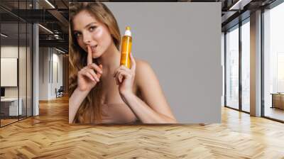 Half-naked woman showing silence gesture while showing beauty product Wall mural