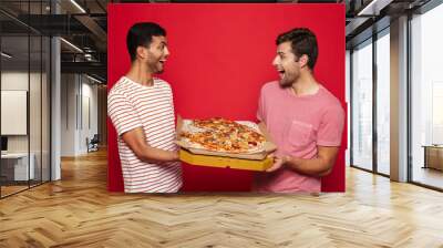 Handsome happy young men friends isolated over red wall background holding big pizza. Wall mural