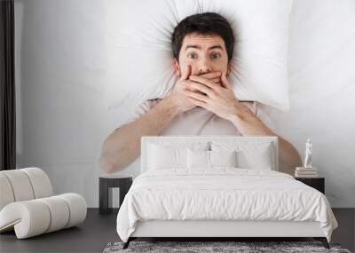 Handsome young man in the morning under blanket in bed lies make covering mouth. Wall mural