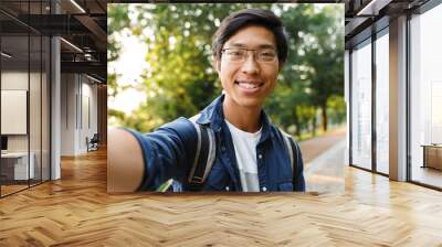 Happy asian male student in eyeglasses making selfie Wall mural