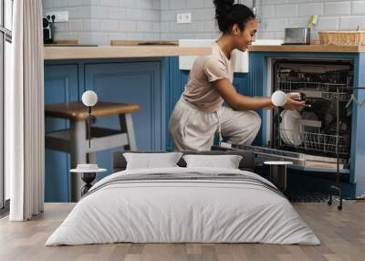 Happy black woman smiling while using dishwasher at home kitchen Wall mural