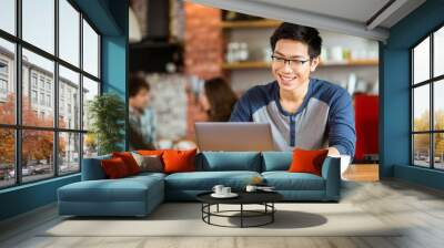 happy cheerful asian male smiling and using laptop in cafe Wall mural