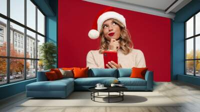 Happy cute girl in santa hat holding mobile phone Wall mural