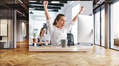 Happy excited business woman in office working with computer make winner gesture. Wall mural