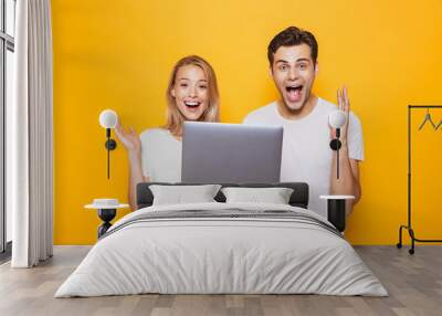 Happy excited young loving couple isolated over yellow wall background using laptop computer. Wall mural