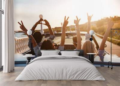 Happy friends in cabriolet with raised hands driving on sunset Wall mural