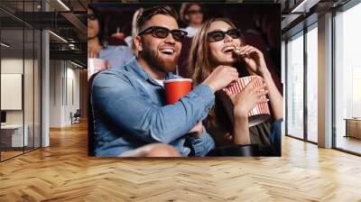 Happy friends sitting in cinema watch film eating popcorn Wall mural