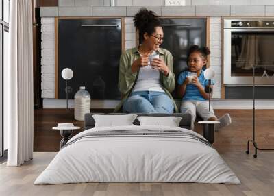 Happy mother sitting on floor with her daughter in home kitchen Wall mural