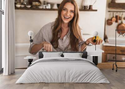 Happy positive cute beautiful woman indoors at the kitchen cooking. Wall mural