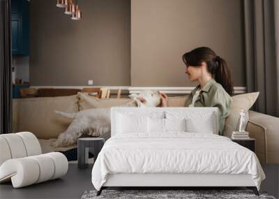 Happy white woman reading book while resting with her dog on sofa Wall mural