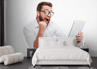 Happy young bearded man using tablet computer make winner gesture. Wall mural