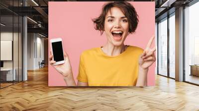 Happy young beautiful woman posing isolated over pink wall background using mobile phone. Wall mural