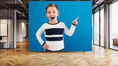 Happy young boy pointing up and holding arm on hip Wall mural