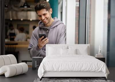 Happy young brunette man holding mobile phone Wall mural