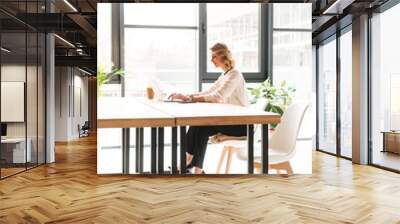 Happy young business woman sitting in office using laptop Wall mural