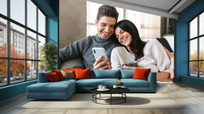 Happy young couple sitting on a couch at home Wall mural