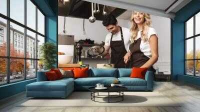 Happy young friends loving couple chefs on the kitchen cooking. Wall mural