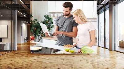 Happy young loving couple standing at kitchen and cooking Wall mural