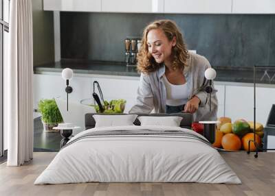 Happy young woman making a salad at the kitchen Wall mural